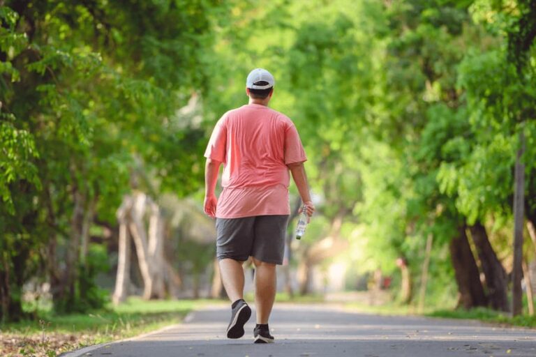 Leveraging summertime for weight loss - bariatric surgery. image of a man in a sweaty shirt walking outdoors in a park with a water bottle.